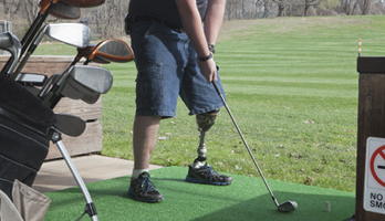 Man with a prosthetic leg swinging a golf club.