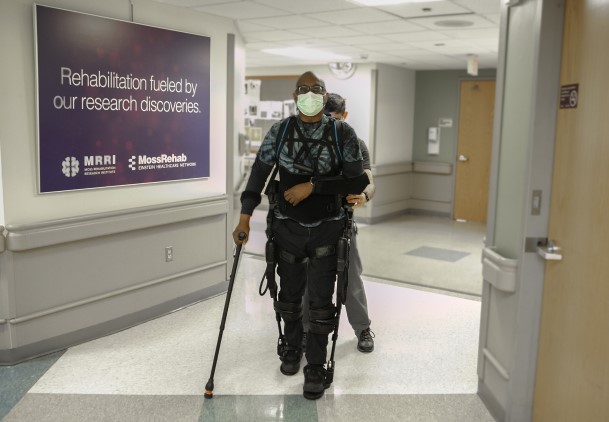 A patient wearing a lower extremity exoskeleton, arm sling, and crutch.  