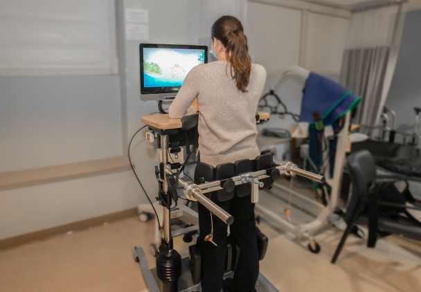A patient strapped to device which helps her stand and balance.