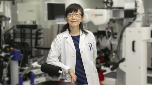 Dr. Ning Cao standing next to rehab robots