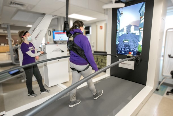 A patient walking on a treadmill front of a large LCD screen