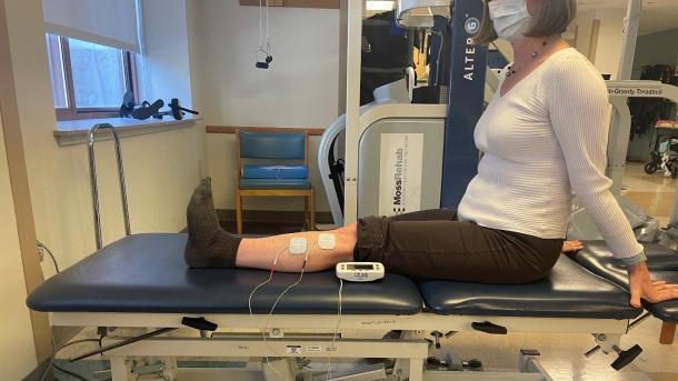 Woman sitting a mat table with electrodes attached to her leg.