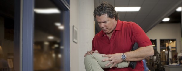 A man in a red shirt helping an woman with a leg stretch.