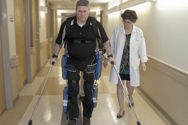 A man wearing the ReWalk Restore exo-suit walking next to a clinician.