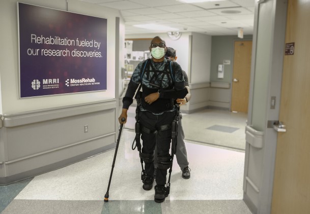 A patient wearing a lower extremity exoskeleton, arm sling, and crutch.